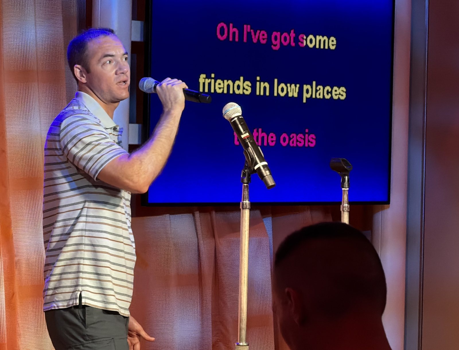 Guest singing karaoke into a wireless microphone with lyrics displayed behind him